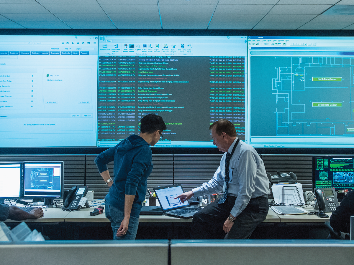 people looking at a laptop in building's access control room